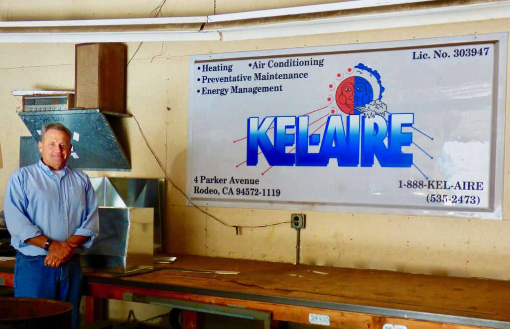 Man beside Kel-Aire sign on wall